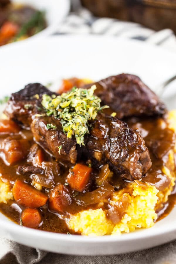 Braised short ribs with carrots in sauce on polenta, topped with rosemary lemon gremolata.