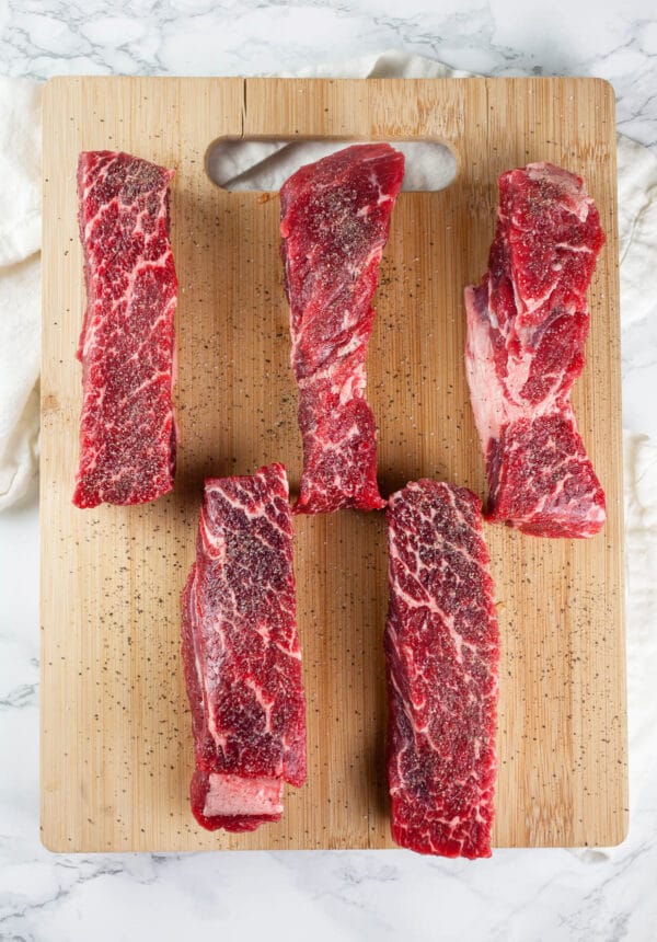 Boneless beef short ribs with salt and pepper on wooden cutting board.