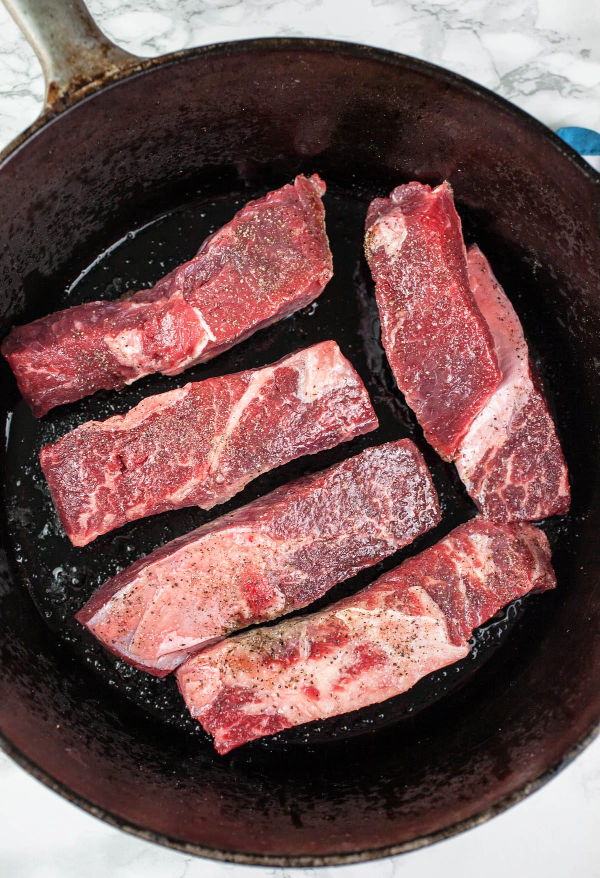 Raw boneless short ribs seared in cast iron Dutch oven.