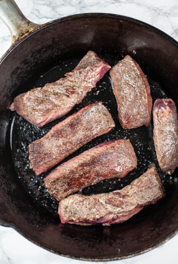 Seared boneless beef short ribs in cast iron Dutch oven.