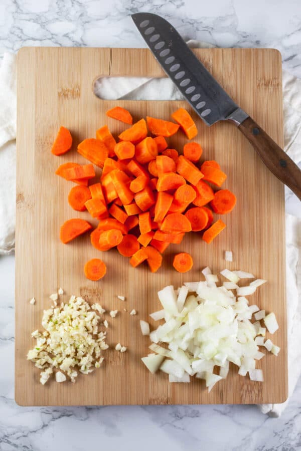 Minced garlic and onions and sliced carrots on wooden cutting board.