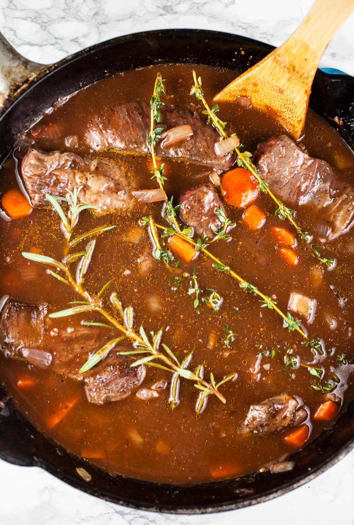 Beef broth, meat, and fresh herbs in cast iron Dutch oven.