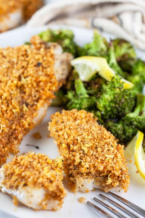 Panko baked cod with broccoli and lemon slices on white plate.
