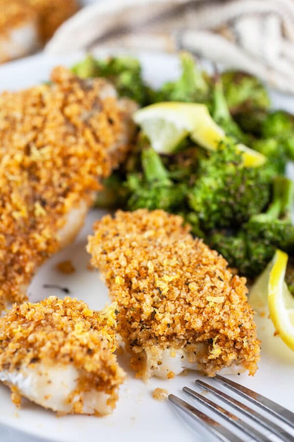 Panko crusted cod with broccoli and lemon slices on white plate.