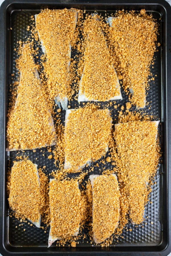 Unbaked cod fillets topped with Panko breadcrumb coating on baking sheet.