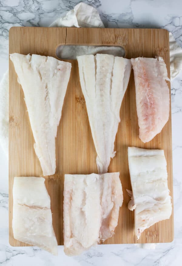 Uncooked cod fillets on wooden cutting board.