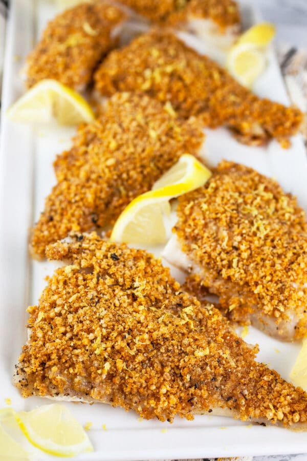 Panko baked cod fillets on white serving platter with lemon slices.