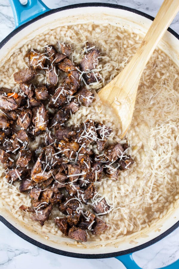 Diced beef short ribs and Parmesan cheese with Arborio rice in white cast iron skillet.