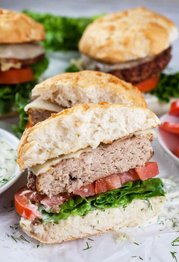 Turkey burgers on buns with lettuce, tomato, and dill aioli cut in half.