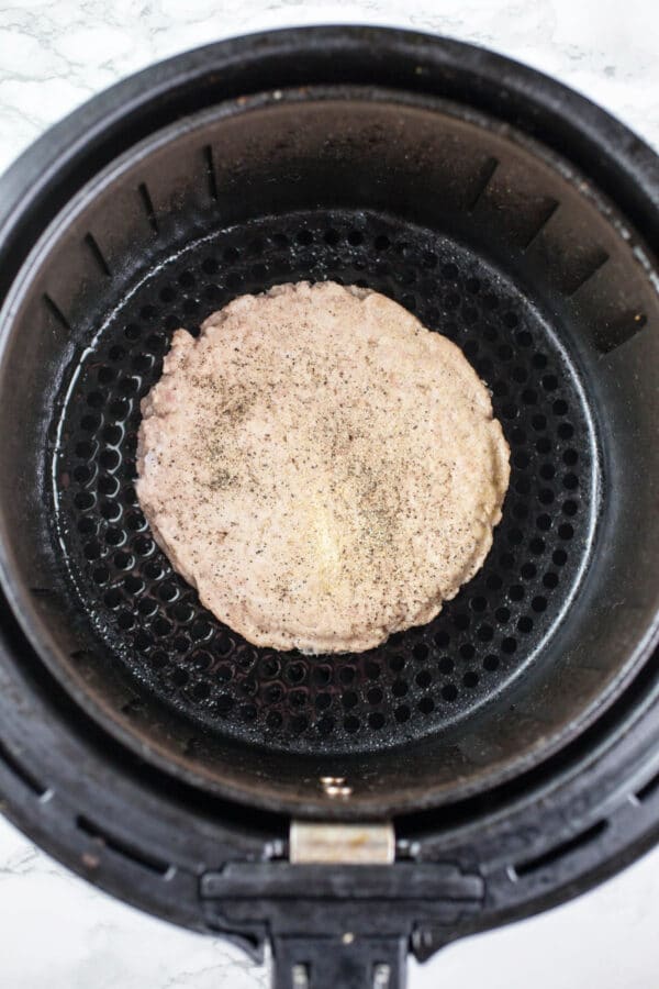 Frozen turkey burger in air fryer basket.