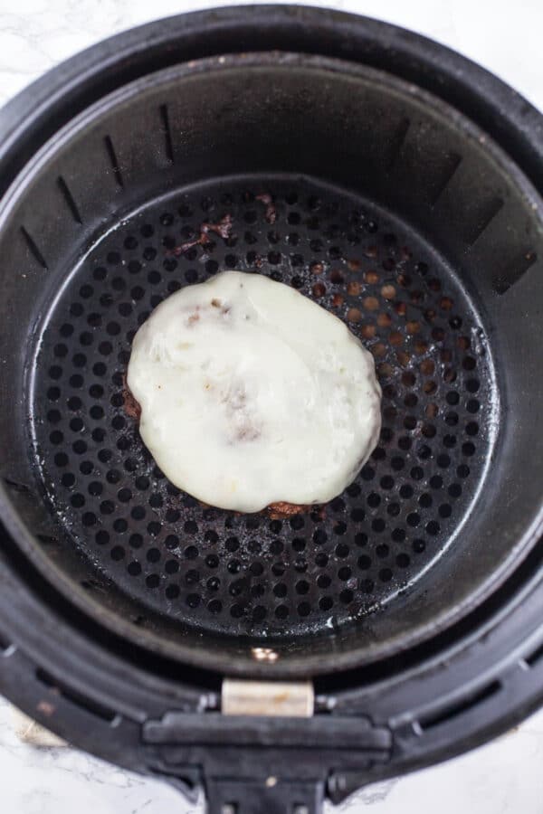 Cooked turkey burger patty with provolone cheese in air fryer basket.