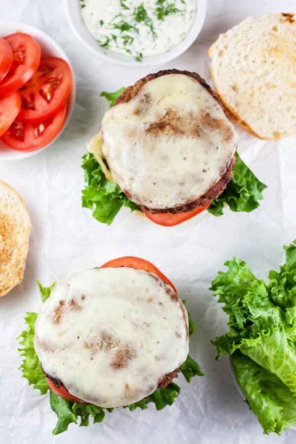 Open face turkey burgers with melted cheese on buns with lettuce and tomatoes.