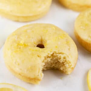 Baked lemon doughnut with bite taken out on white surface.