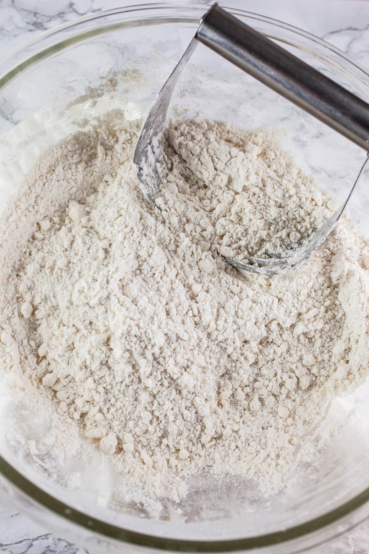 Butter and dry ingredients cut together with metal pastry cutter in glass mixing bowl.