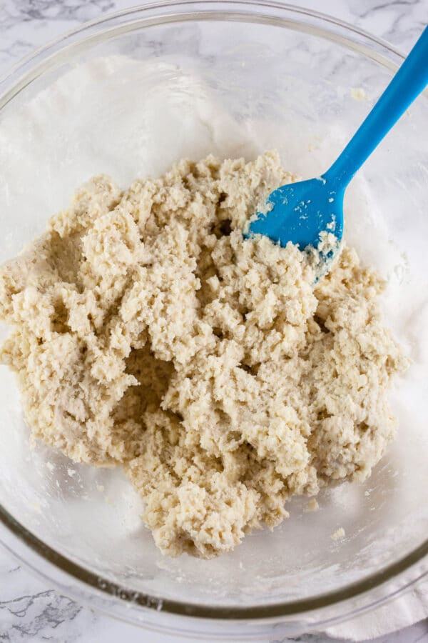 Biscuit dough in large glass mixing bowl with blue spatula.