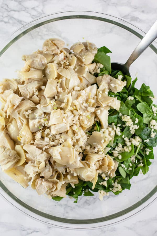 Chopped garlic, spinach, and artichoke hearts in large glass mixing bowl.