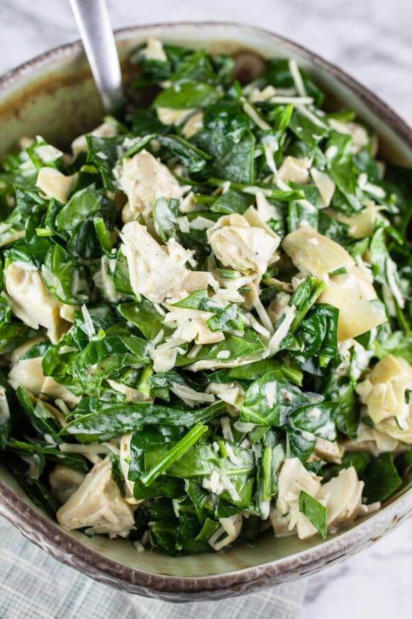This Lemony Spinach Artichoke Dip is a lightened up version of the classic! This recipe is so easy to make and uses fresh spinach and artichokes. It's light and lemony and focuses on the flavor of the ingredients. This simple appetizer is perfect for those who want a healthy version of this iconic dip. Makes enough to feed a crowd so it's great for picnics or parties! #spinachartichokedip #spinach #artichoke #dips #appetizers #recipes #healthy Fresh spinach artichoke dip with Parmesan cheese in ceramic bowl.