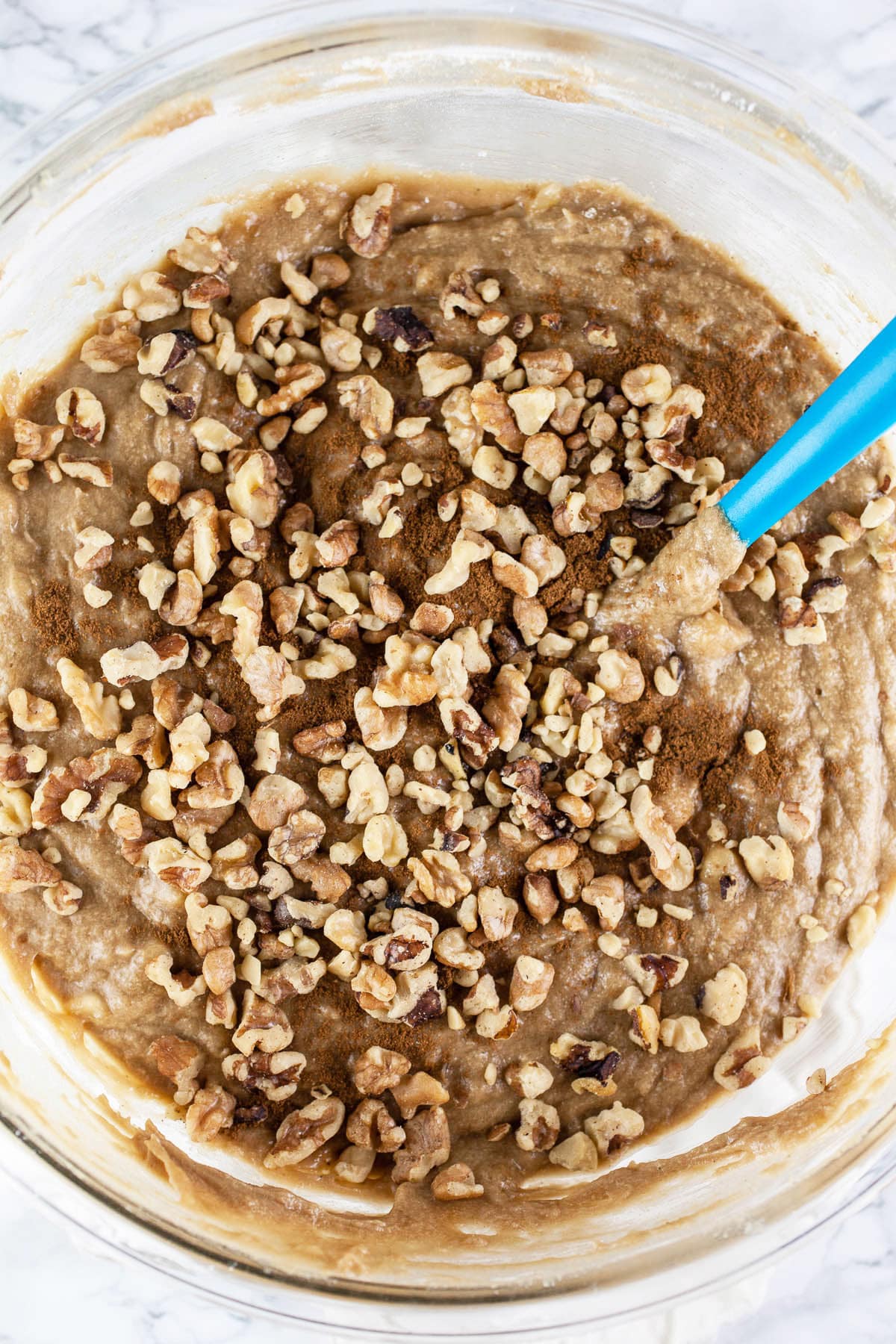 Banana bread batter with cinnamon and walnuts in large glass mixing bowl.