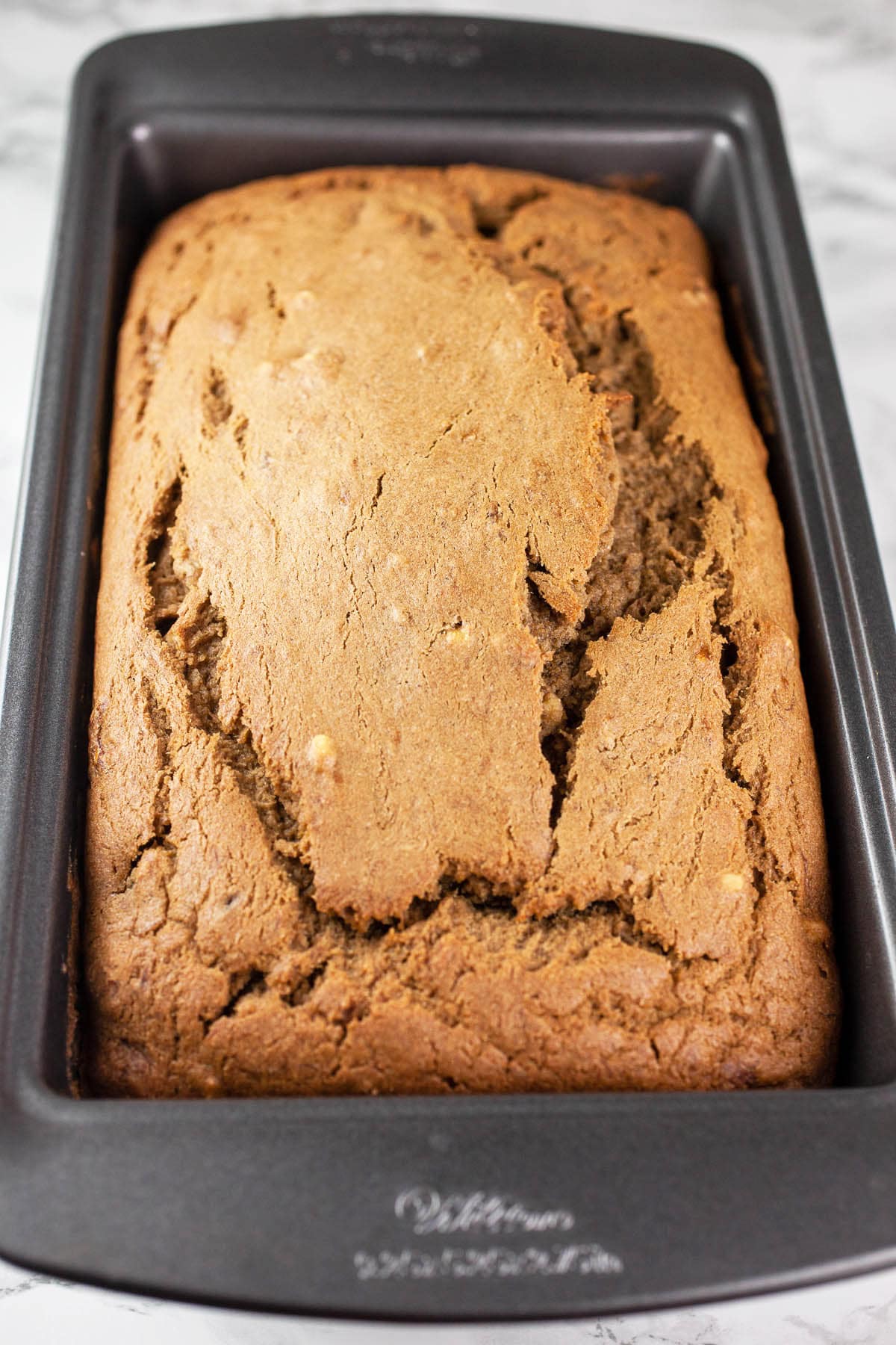 This Coffee Infused Banana Bread is the best banana bread recipe ever! It's easy to make and accented with a rich coffee flavor. This banana bread is moist and great for breakfast, desserts, or an after dinner treat. It's homemade and full of cinnamon, walnut, and banana flavor. I love these simple quick breads when it comes to baking! #bananabread #coffee #recipes #desserts #homemade #banana #bread Baked banana bread in metal loaf pan.