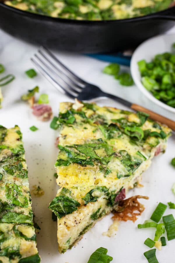 This Ham, Cheese, and Asparagus Frittata recipe is super easy to make and is perfect for breakfast, brunch, or anytime! It's full of smoky ham, asparagus, fresh spinach and, of course, eggs. This frittata recipe is hearty and healthy. It's also a great way to use up leftover holiday ham or vegetables in the fridge. #frittata #ham #asparagus #breakfast #lunch #dinner #recipe Ham and cheese frittata with spinach garnished with green onions.