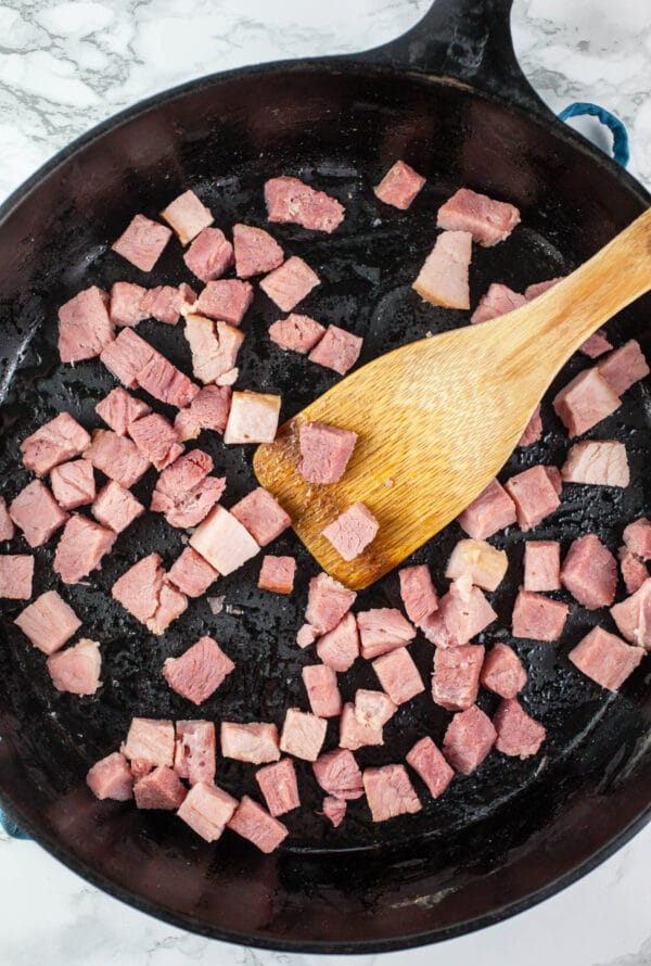 Diced ham sautéed in cast iron skillet with wooden spatula.