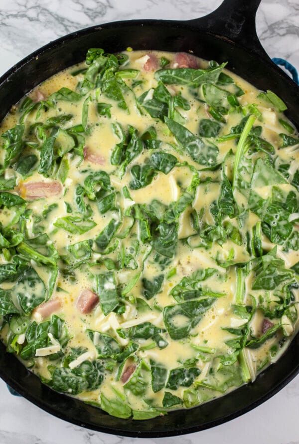 Uncooked ham, asparagus, and spinach frittata in cast iron skillet.