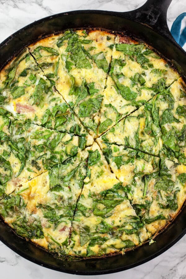 Baked ham, asparagus, and spinach frittata cut into slices in cast iron skillet.