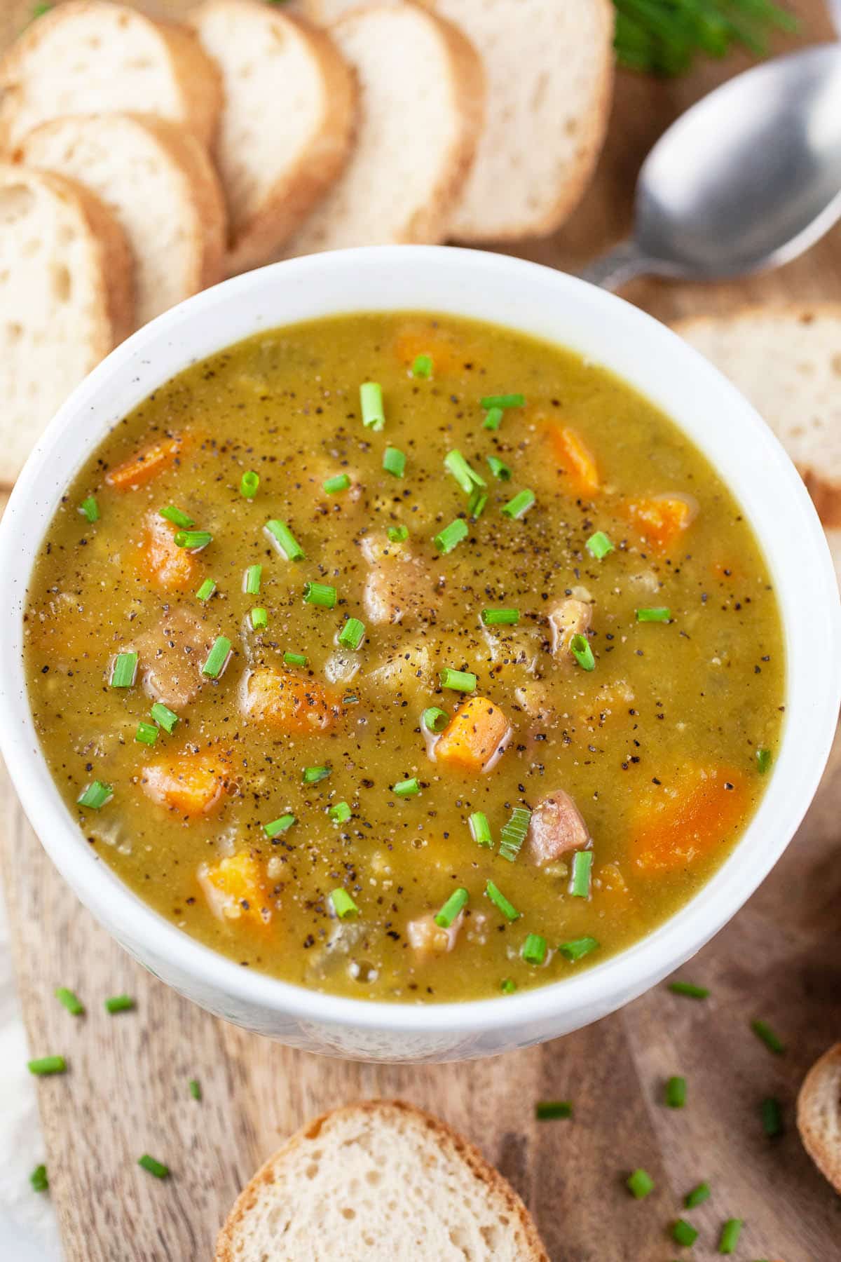 Split pea ham soup in white bowl with bread slices and chives.