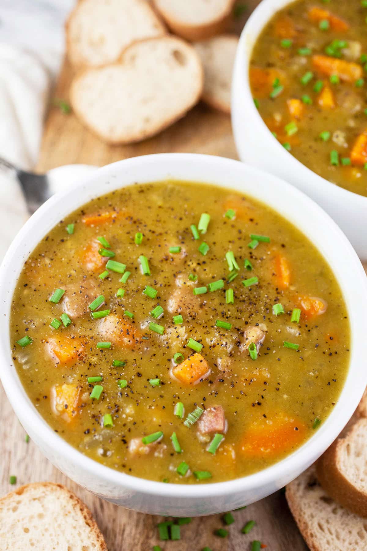 Split pea ham soup on wooden serving board with slices of bread.