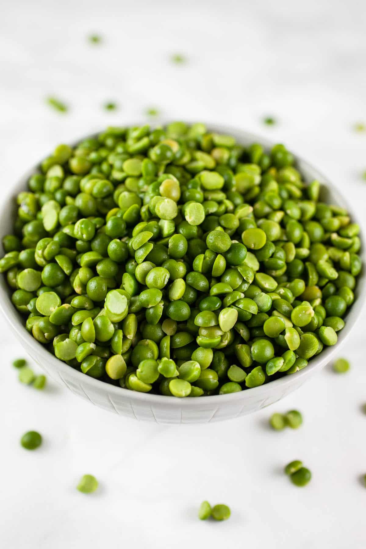 Uncooked split peas in small bowl on white surface.