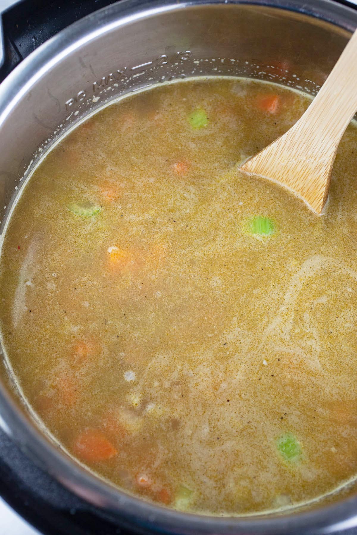 Uncooked split pea ham soup in Instant Pot with wooden spoon.