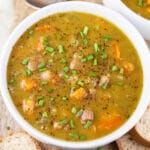 Split pea and ham soup garnished with minced chives in white bowl.
