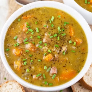 Split pea and ham soup garnished with minced chives in white bowl.