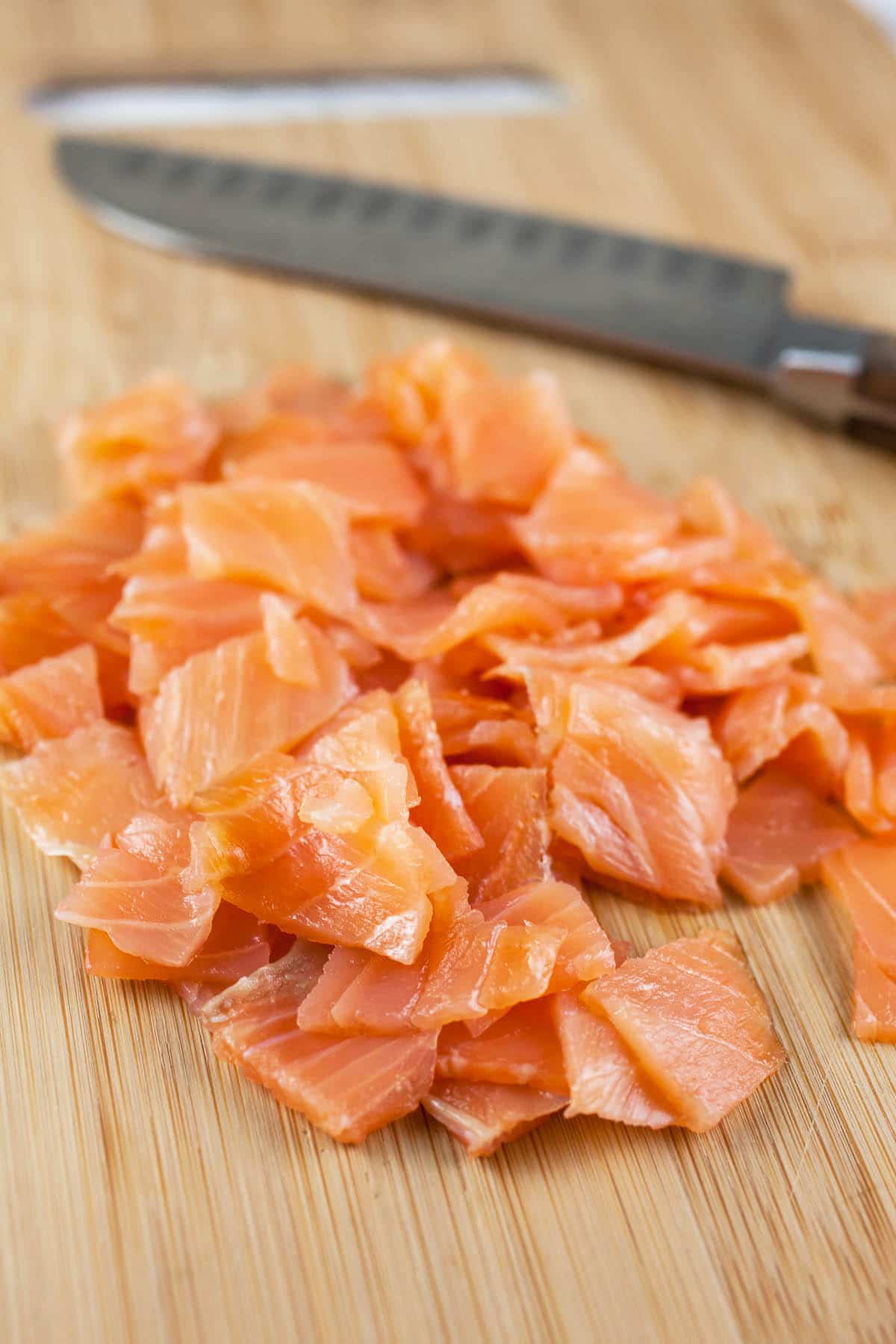 Sliced smoked salmon on wooden cutting board with knife.