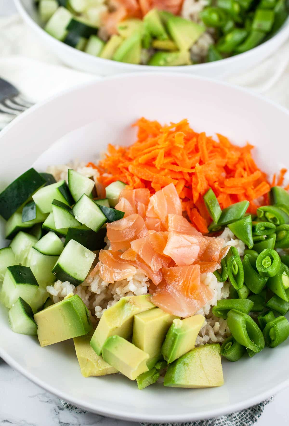 Diced avocado, snap peas, carrots, cucumber, and smoked salmon in white bowls.