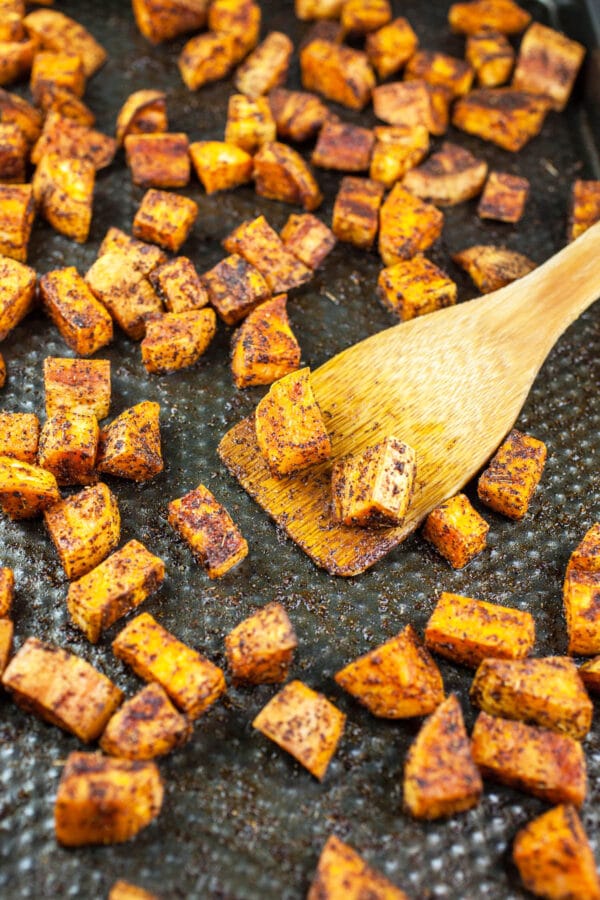 Roasted sweet potatoes on baking sheet with wooden spatula.