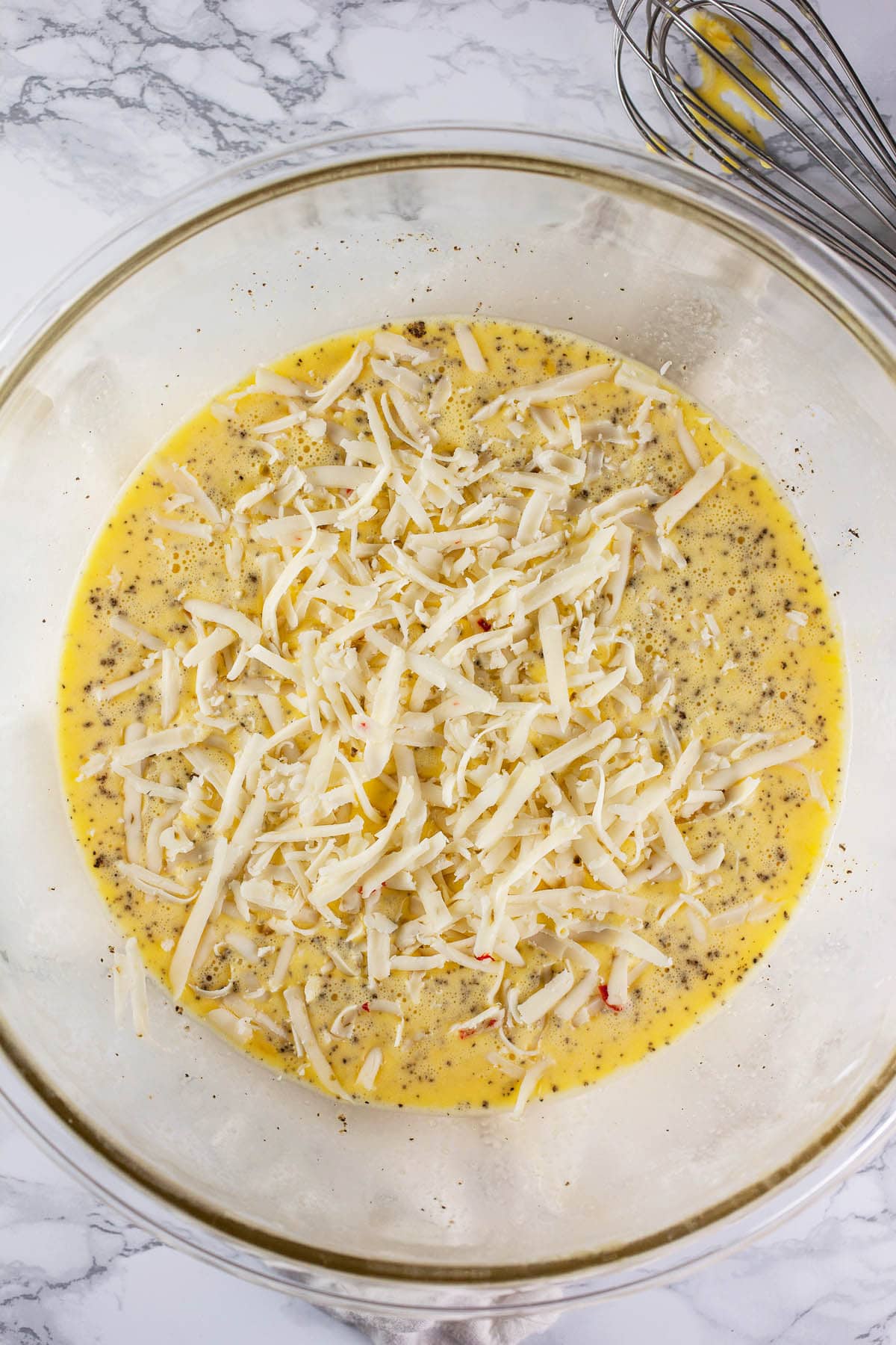 Whisked eggs with shredded cheese in large glass mixing bowl.