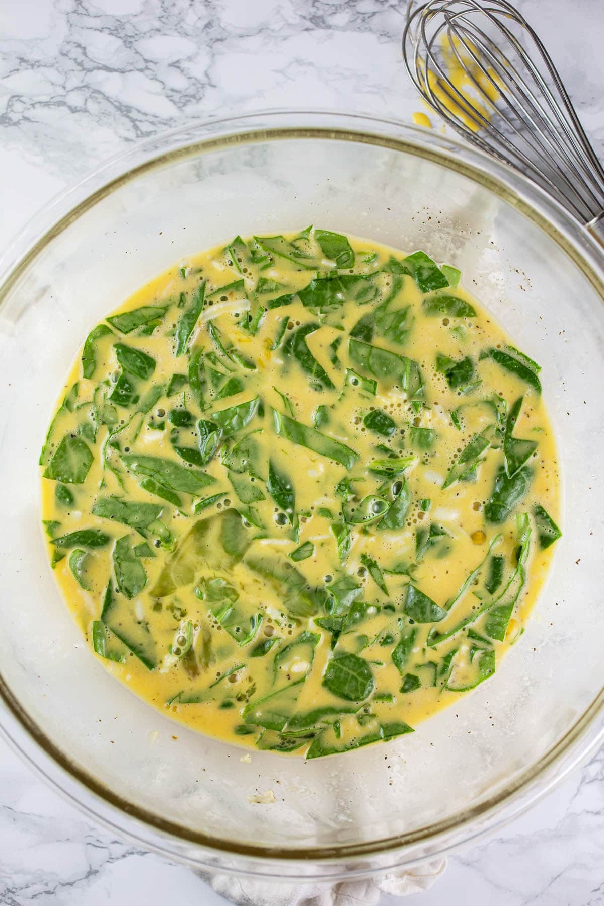 Egg mixture with chopped spinach in large glass mixing bowl.
