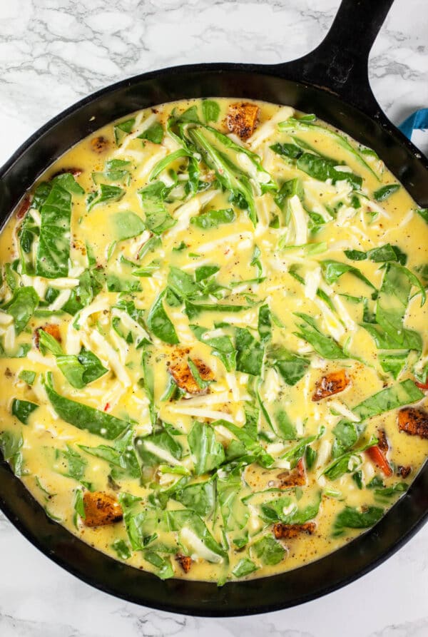 Egg mixture, spinach, cheese, and sweet potatoes in cast iron skillet.