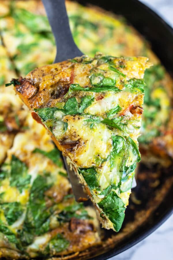 Slice of Southwest frittata lifted from cast iron skillet on metal spatula.