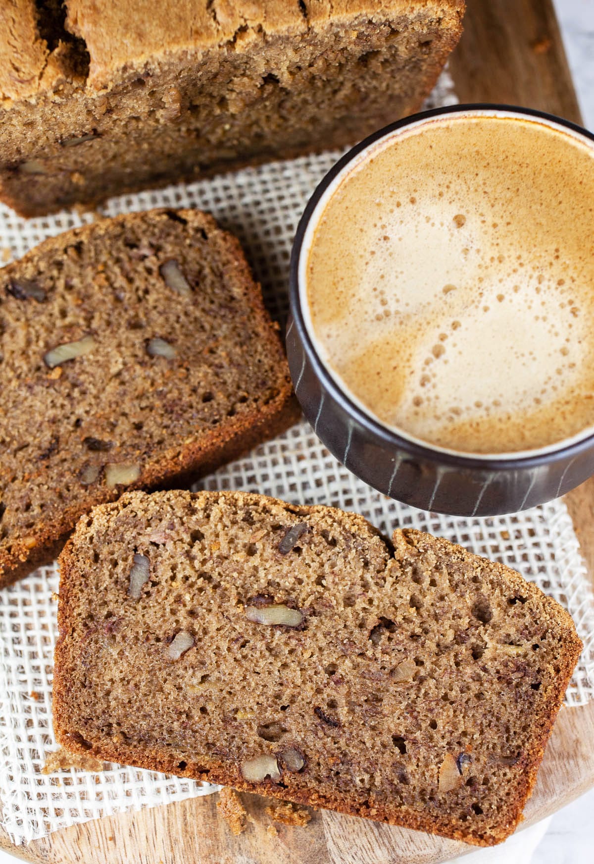 This Coffee Infused Banana Bread is the best banana bread recipe ever! It's easy to make and accented with a rich coffee flavor. This banana bread is moist and great for breakfast, desserts, or an after dinner treat. It's homemade and full of cinnamon, walnut, and banana flavor. I love these simple quick breads when it comes to baking! #bananabread #coffee #recipes #desserts #homemade #banana #bread Banana bread on wooden board with cup of coffee.