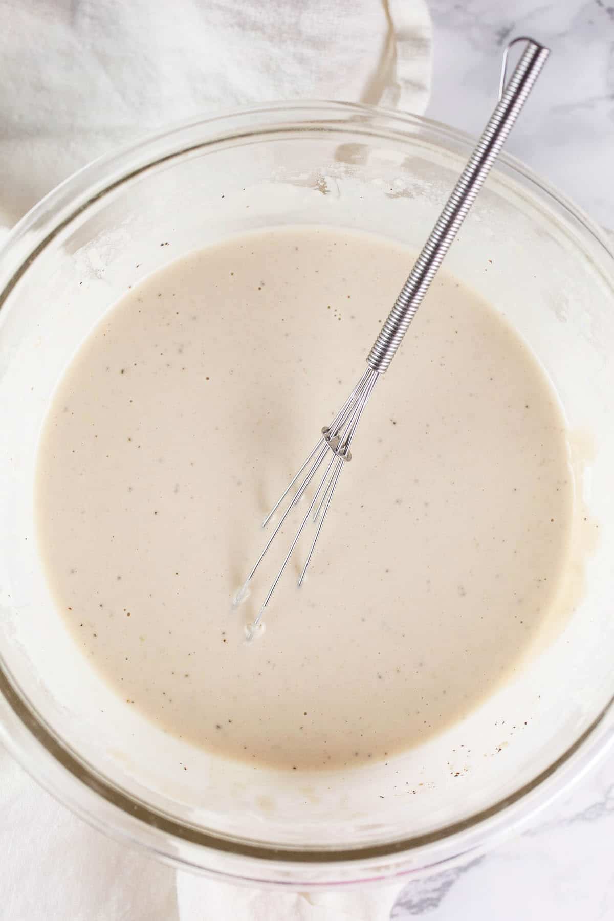 Tahini sauce in small glass bowl with whisk.