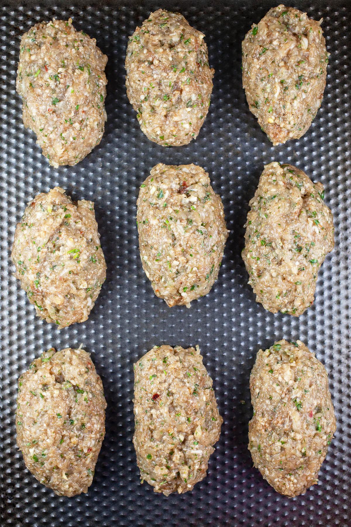 Raw kofta kebabs on baking sheet.