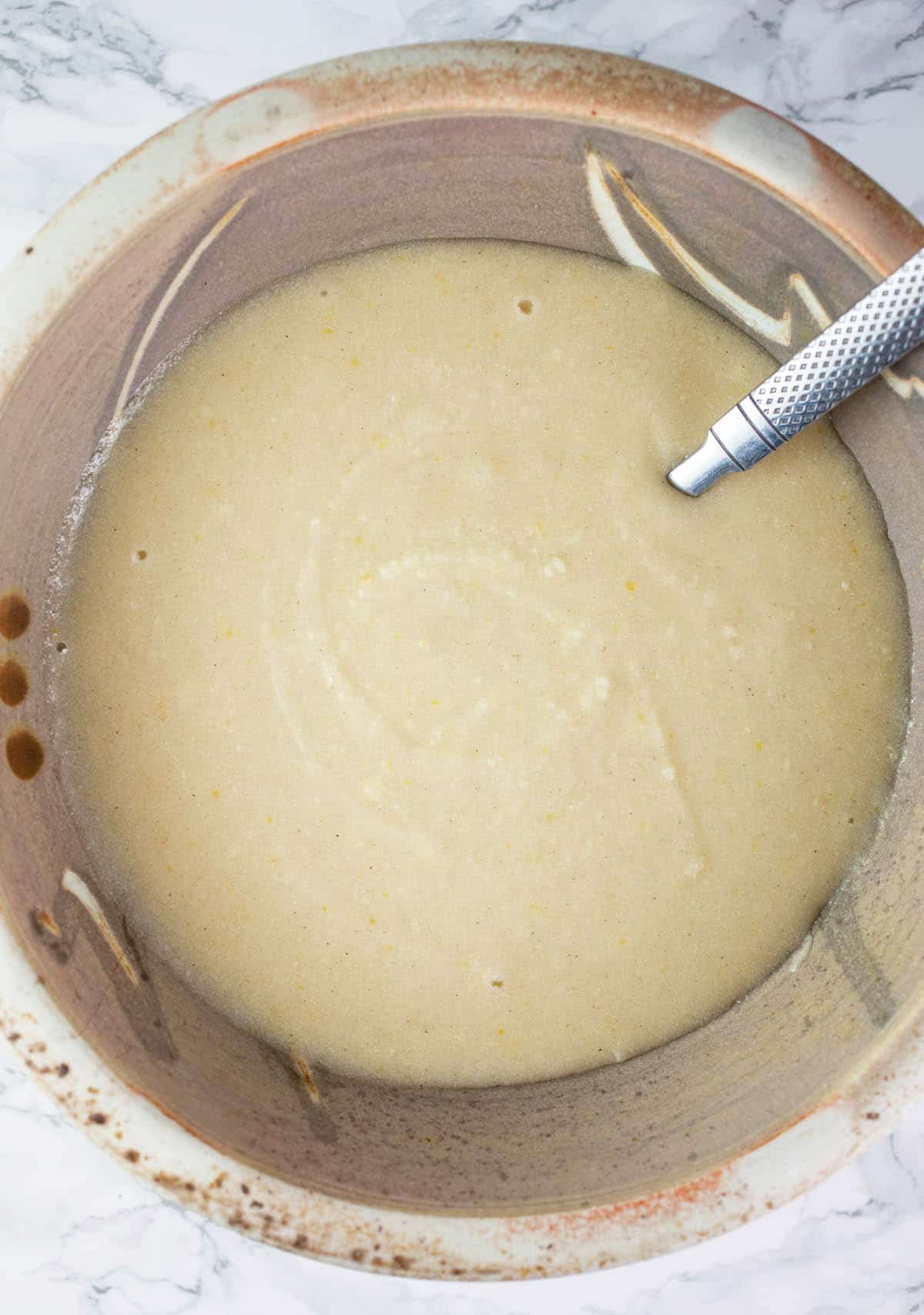 Almond cake batter with melted butter added in ceramic bowl.