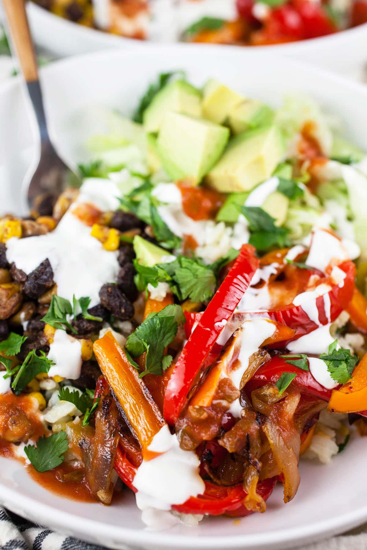 Vegetarian fajita bowl with bell peppers, black beans, corn, avocado, sour cream, and salsa.