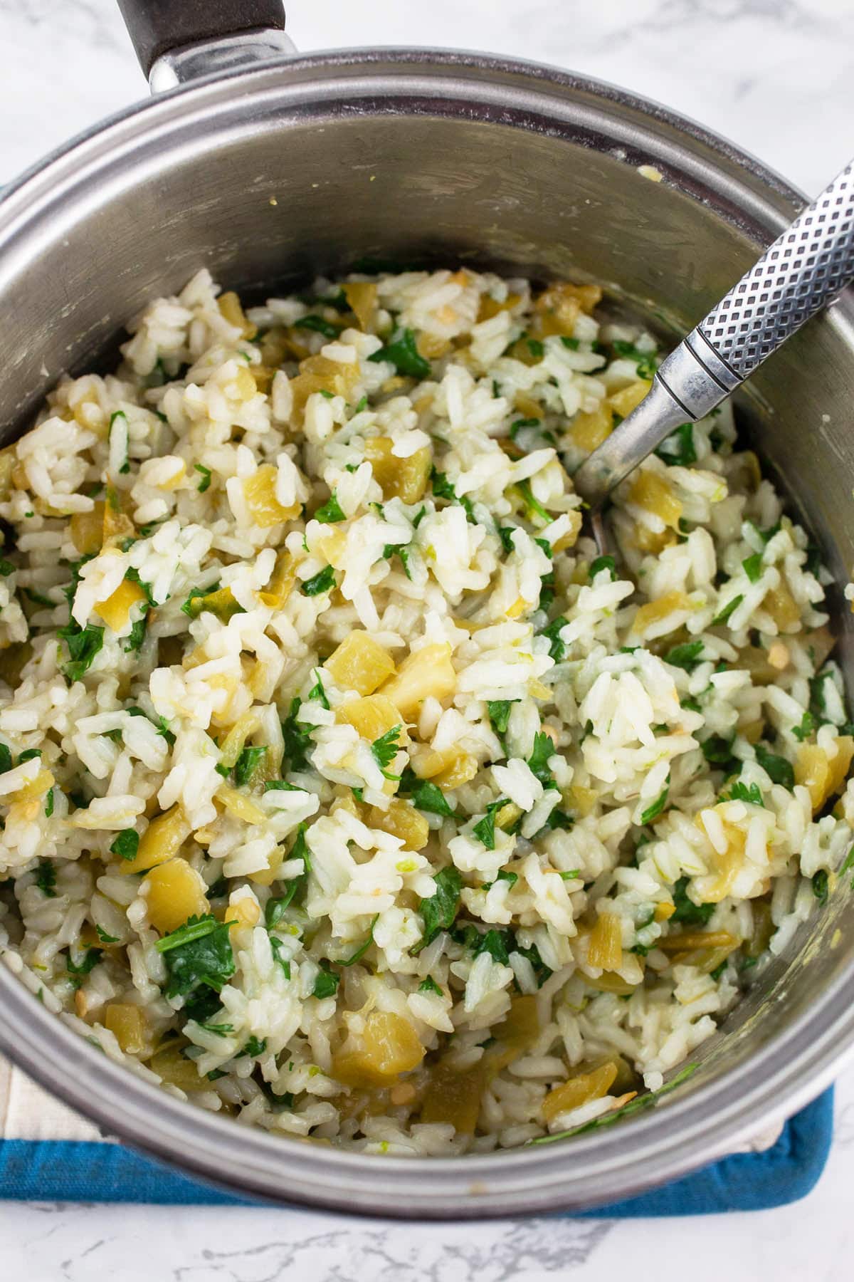 Cooked white rice with diced green chilis, lime zest, and cilantro in small pan.