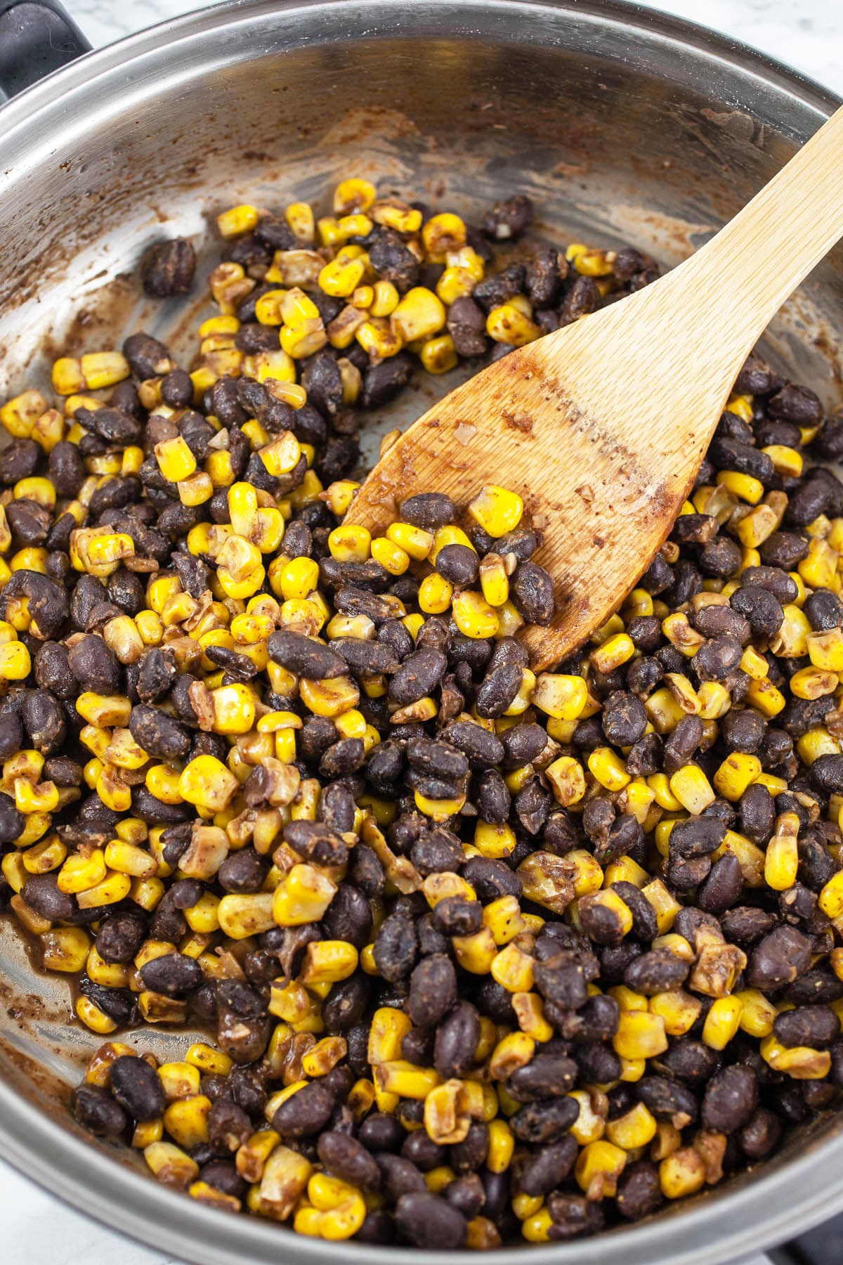 Black beans and corn sautéed in skillet with wooden spoon.