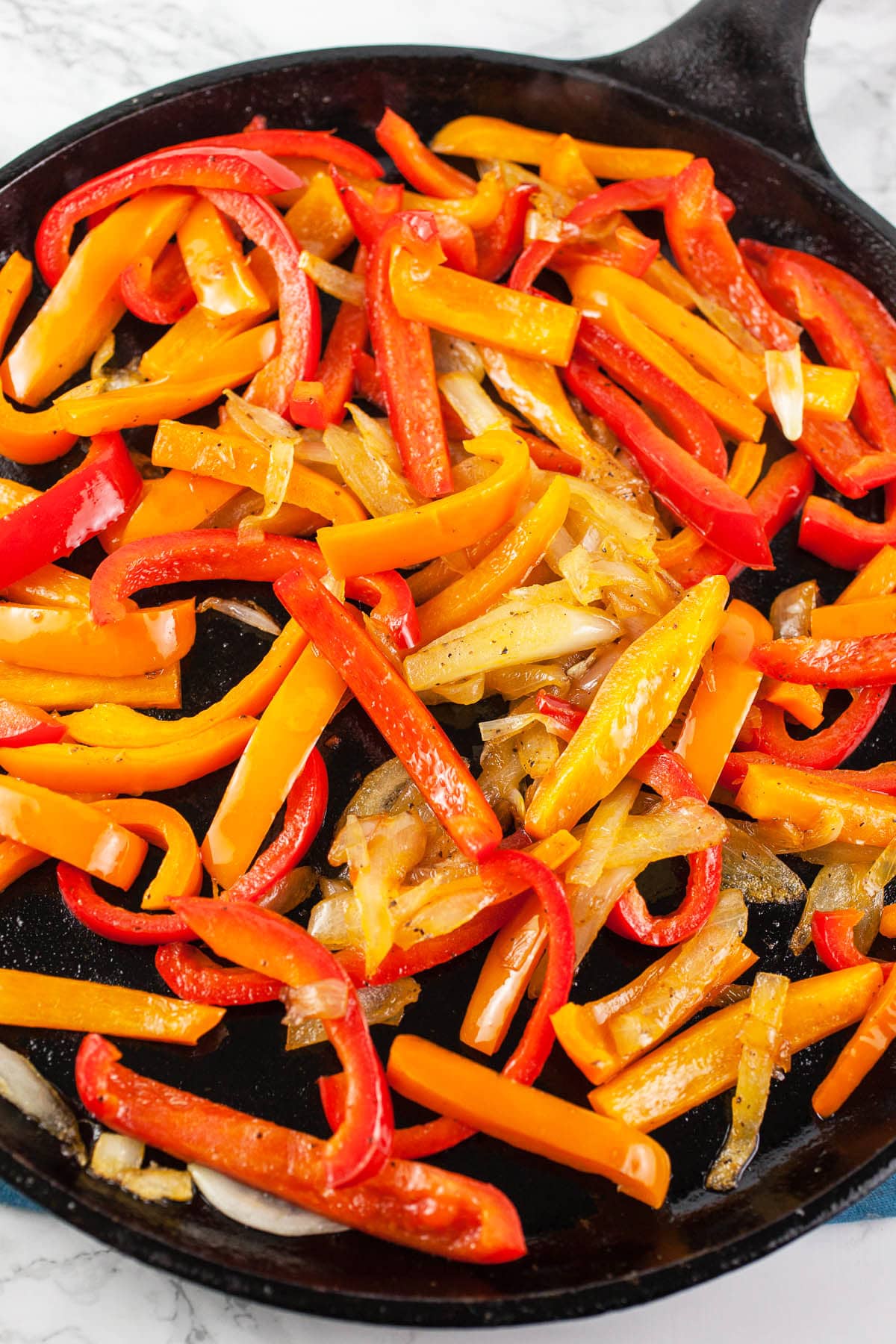 Sliced onions and red and orange bell peppers sautéed on flat cast iron skillet.