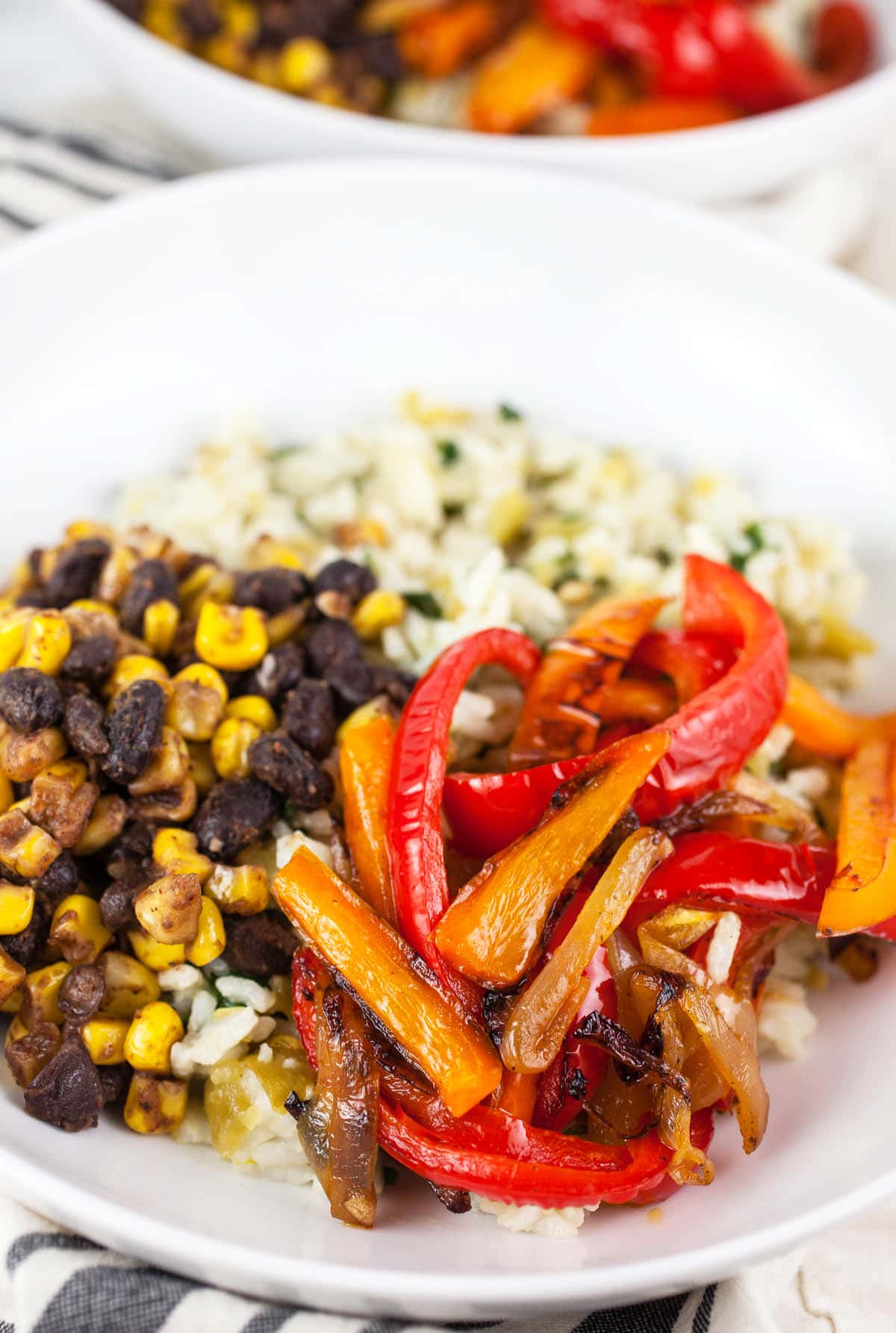 Seared onions, red and orange bell peppers, black beans, corn, and rice in white bowls.
