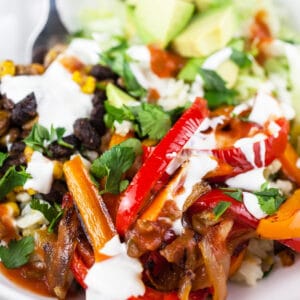 Vegetarian fajita bowls with bell peppers, black beans, corn, avocado, sour cream, and salsa.